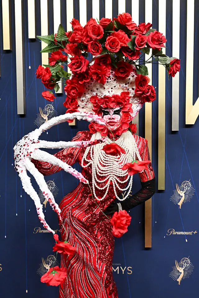 Drag queen Lucky Starzzz in a an intricate outfit featuring giant bedazzled claws, a red sequined dress, and a bouquet of roses on top