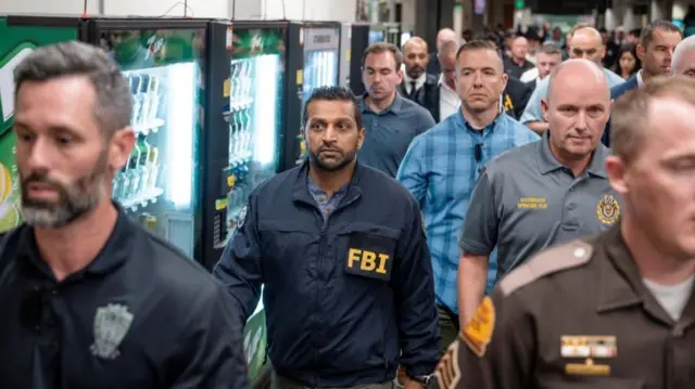 Kash Patel in an FBI jacket, walking with other officials down a hallway.