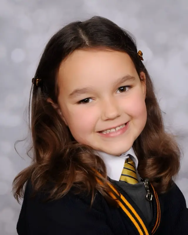 Bebe King, who has long wavy brown hair, smiles at the camera in her black school uniform