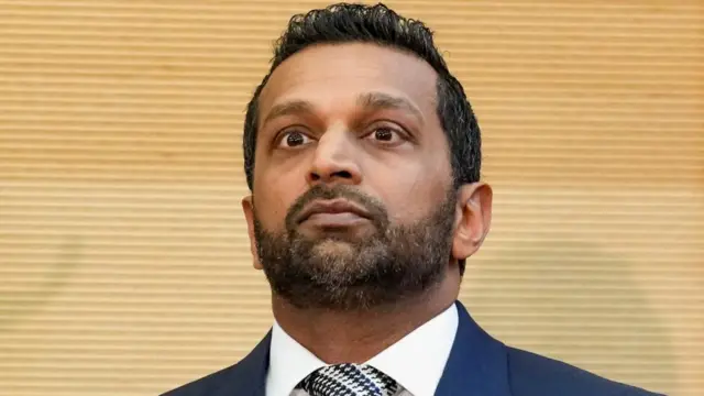 Kash Patel from his shoulders up in front of a yellow background