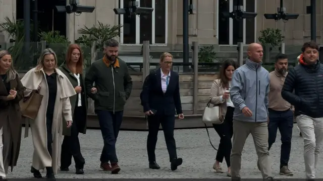 A group of people walking across a stone square, some linking arms
