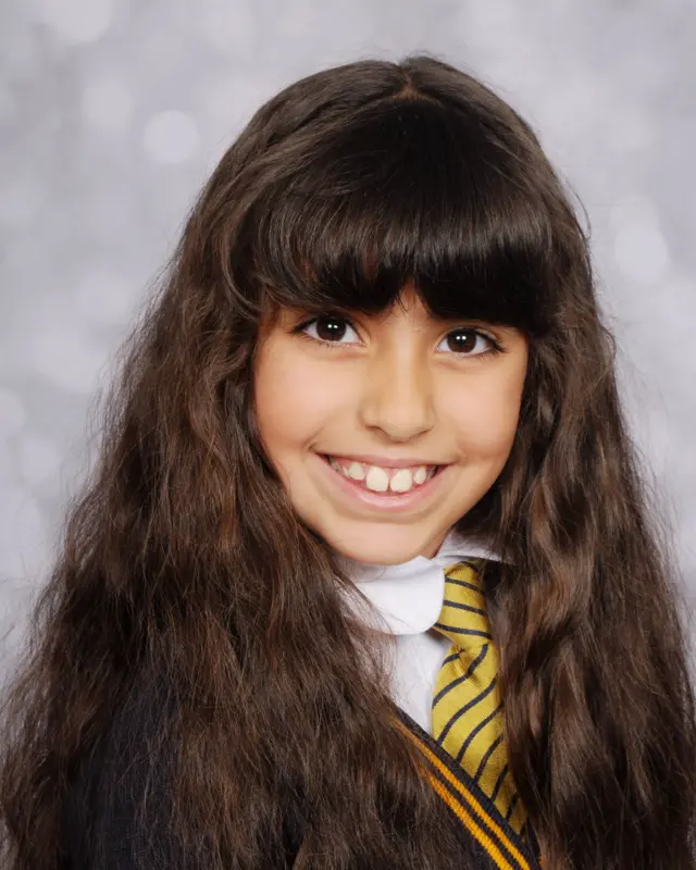 Alice Aguiar, with long dark brown hair, smiles at the camera in her school uniform