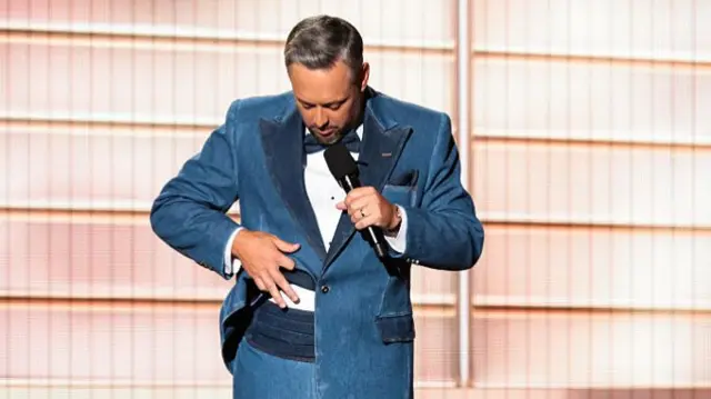 Nate Bargatze looking down and touching his blue denim suit