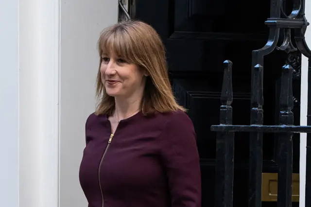 Rachel reeves leaves No.10 Downing Street. She is wearing a dark jacket and the iconic black door can be seen behind her.