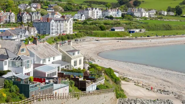 General view of the seaside town of Cricieth in north Wales, including a pebble beach and large townhouses overlooking the seafront, in the sunshine.