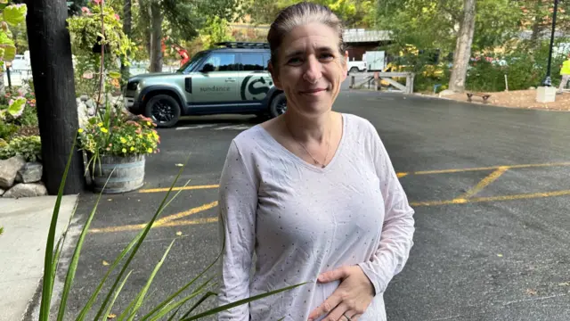 A woman stands in a parking lot and wears a white t-shirt.
