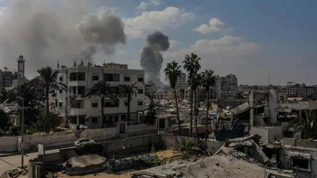 Smoke rises over city of Palm trees and broken buildings