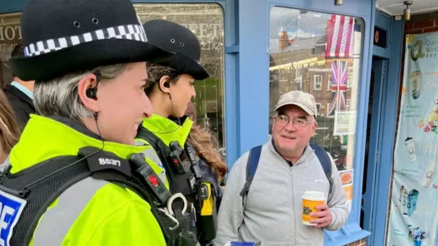 Two police officers stand next to a man holding a coffee