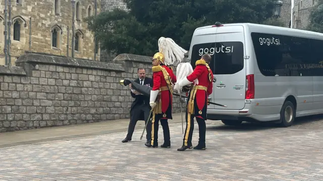 Two members of the guard of honour pack up their equipment in front of a grey people carrier