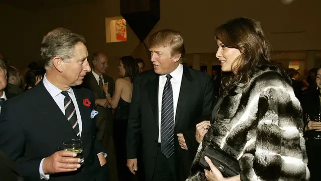 US President Donald Trump talking to King Charles. First Lady Melania Trump stands close by wearing a black and white fur coat.