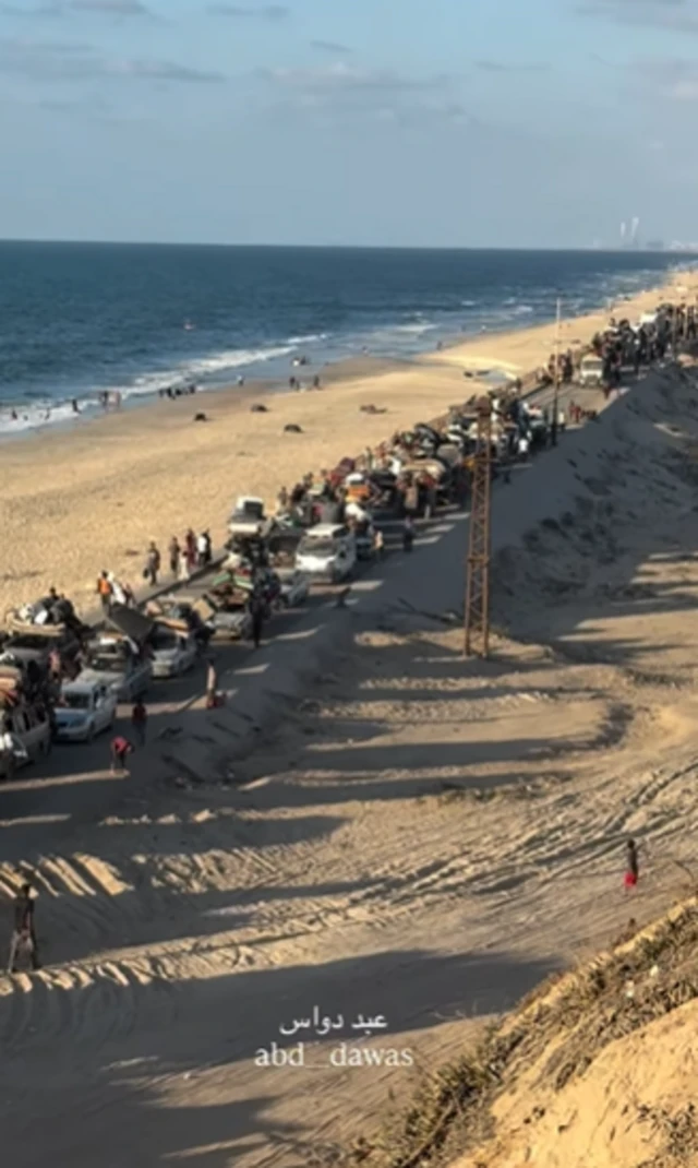 A convoy of vehicles along the al-Rashid road, people are also on foot next to them. The Mediterranean sea is to the left of the road.