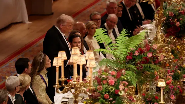Trump stands at the banquet table to deliver his speech. Others seated around him look on