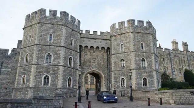 A blue car emerges from the gate of Windsor Castle
