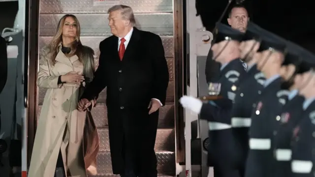 Donald and Melania Trump stand at the bottom of the stairs to Air Force One. In the foreground, soldiers stand in line to greet them.