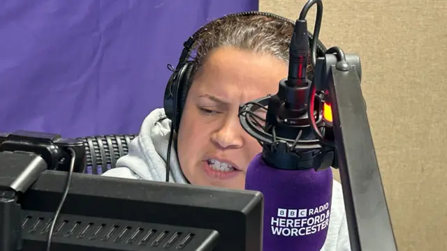 A female radio presenter with dark hair in front of a microphone
