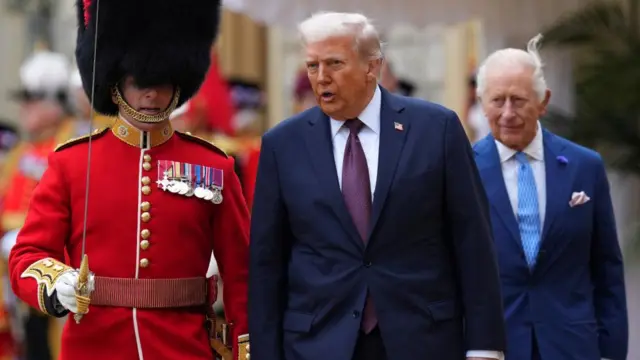 Trump and King Charles walking next to a man in a military uiform.