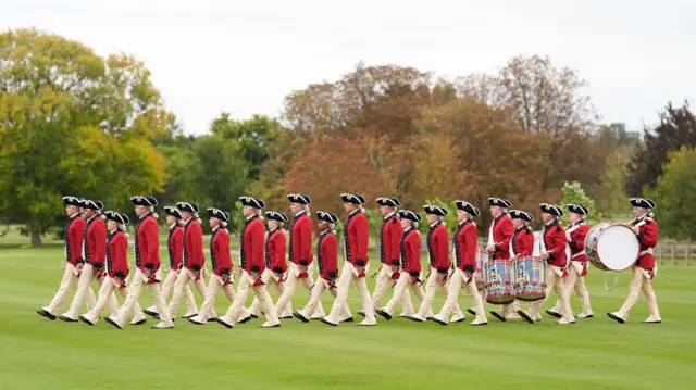 Members of the the United States Army Old Guard Fife and Drum Corps in historic clothing march across the lawn carrying their instruments