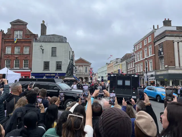 Crowd takes pictures as black US vehicles drive past