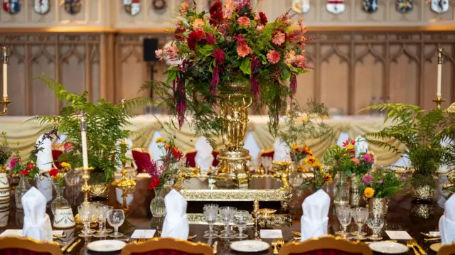 A landscape image of places set for the banquet. The table is decorated with flowers and candles