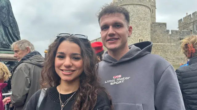 Tyler, left, and Kieran, right, in front of Windsor Castle. Tyler has long brown hair and she is wearing a black jumper. Kieran is taller and he is wearing a grey hoodie.