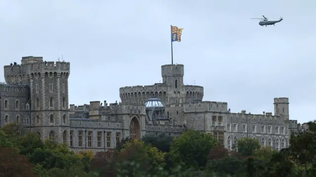 Wide shot of Windsor Castle as Marine One approaches for landing. The King's flag is seen flying on top of a tower
