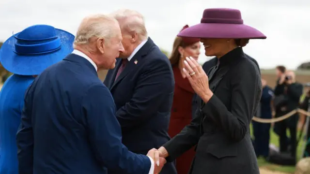 Melania Trump in a wide brimmed purple hat, shaking hands with King Charles.