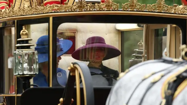 Queen Camilla and US First Lady Melania Trump sit in The Scottish State Coach. A horse is visible in the foreground slightly blurred