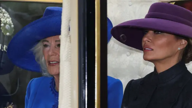 Queen Camilla (L) in blue hat and morning coat dress sits next to Melania Trump (R) in a purple hat and black dress