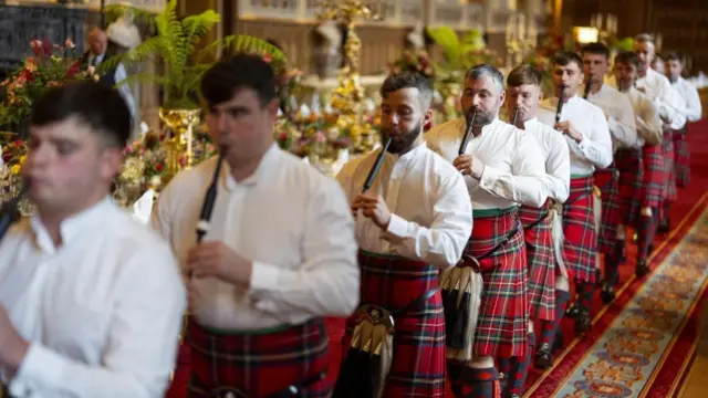 A line of men in kilts playing pipes.