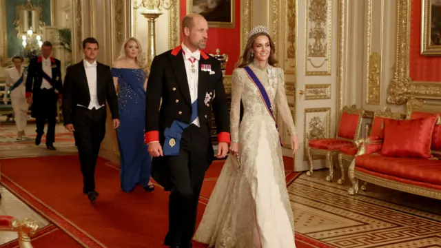 Prince and Princess of Wales walk towards the camera. Others can be seen filing behind them