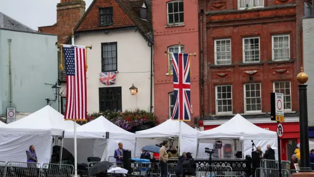 A Union Jack and U.S. flags hang, as media crews setup outside the Windsor Castle