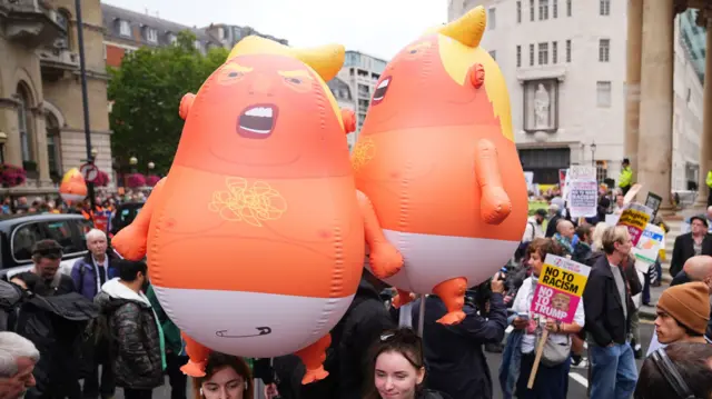 Two balloons depicting a caricature image of Trump as a baby are held up by protesters
