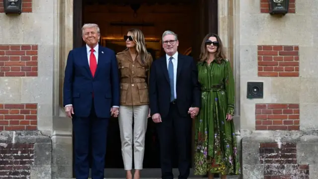 Donald Trump and Melania Trump hold hands, next to them is Keir Starmer and Lady Starmer also holding hands. They are outside Chequers which has stone and brick exterior, they are facing the camera.