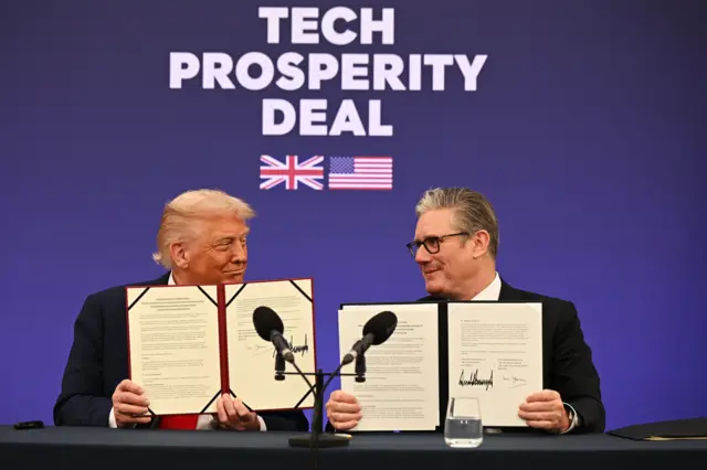 Trump and Starmer smile at one another while holding up signed documents to the cameras