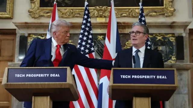 Trump and Starmer stood behind podiums, Trump holds Starmer's back.