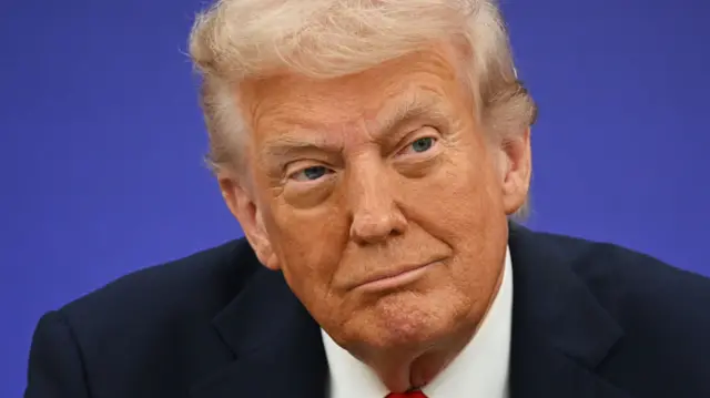 Close up of a satisfied-looking Donald Trump in a black suit, white shirt and red tie looking to his left