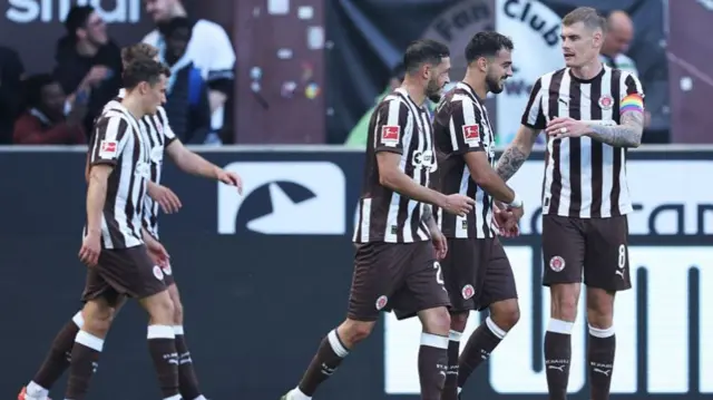 St. Pauli players in black and white kit celebrate a goal together.