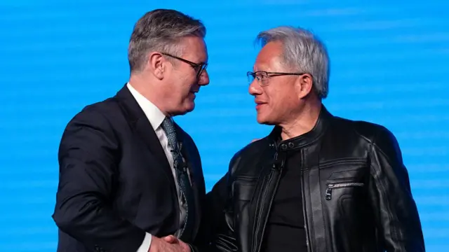 Keir Starmer (L) in a dark suit shakes hands with Jensen Huang, who's in a black leather jacket and black shirt