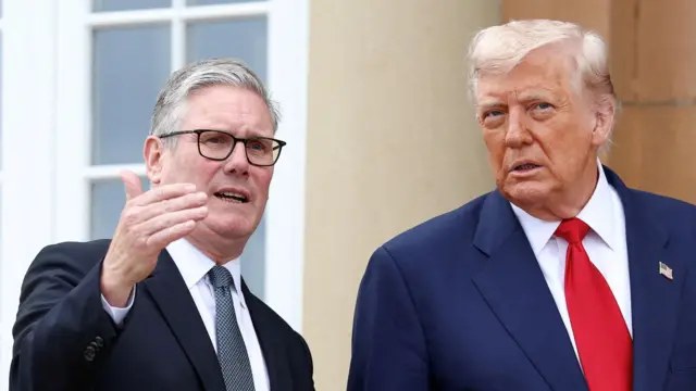 British Prime Minister Keir Starmer (L) gestures with his right hand as he speaks with Donald Trump (R). Both are wearing dark suits, they're standing outside a stone building