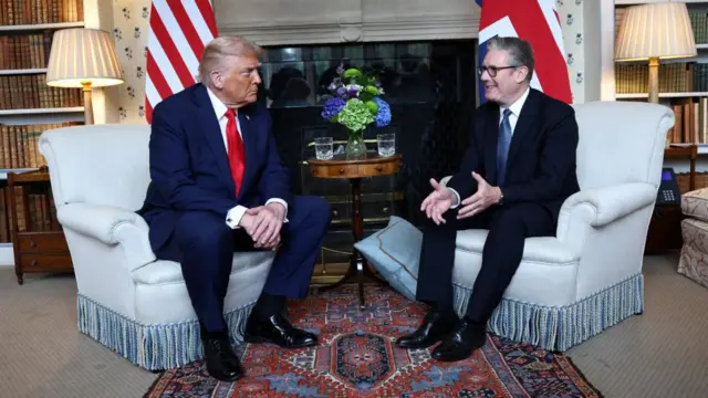 Two men dressed in suits converse on single-seat cream sofas