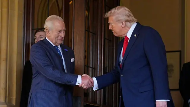Two formally dressed men shake hands in front of a wooden door