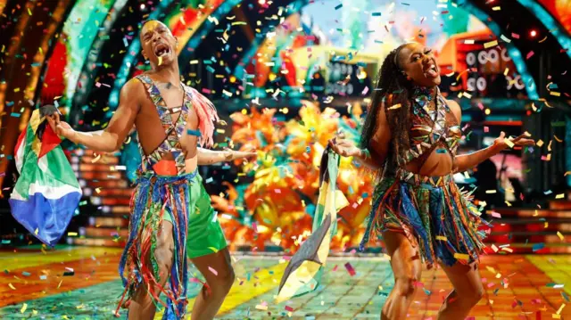 Montell Douglas and Johannes Radebe dancing in carnival outfits with confetti falling on them on the Strictly dance floor