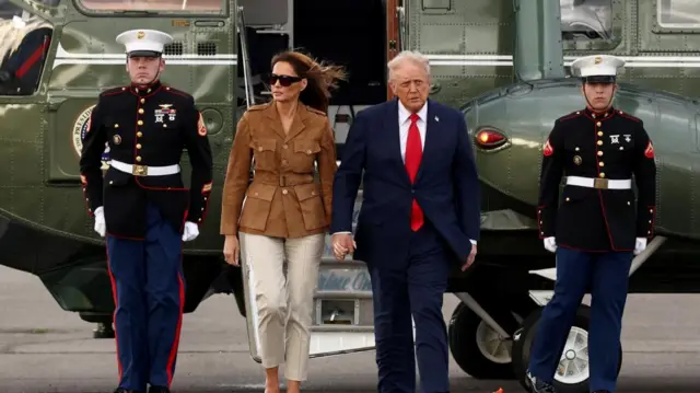 Trump and Melania Trump leaving helicopter, military men next to them.