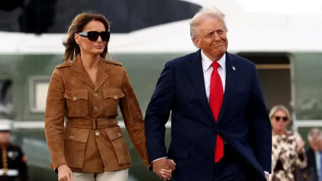 Trump and Melania holding hands walking on runway.