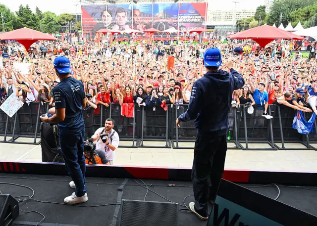 Carlos Sainz and Alex Albon throw caps to the crowd in the fanzone
