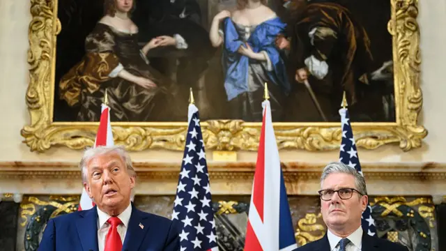 Donald Trump and Keir Starmer sit side-by-side with American and UK flags draped behind them. An oil painting is also seen hanging on the wall behind them.