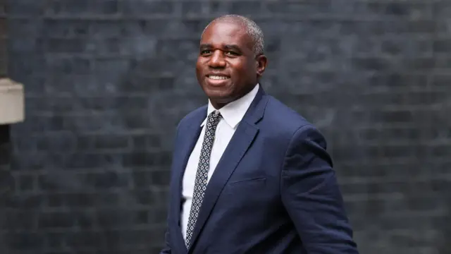 David Lammy wearing suit and patterned tie smiles whilst walking outside