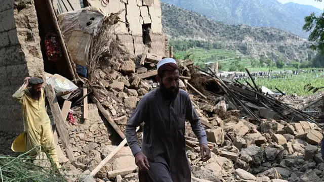 Two Afghan men walking away from a damaged house and rubble