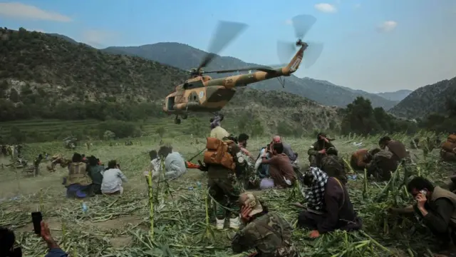 People squat on the ground as a helicopter arrives on a field