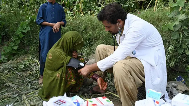 A woman in a green dress and headscarf having her blood pressure taken by a doctor in a white robe
